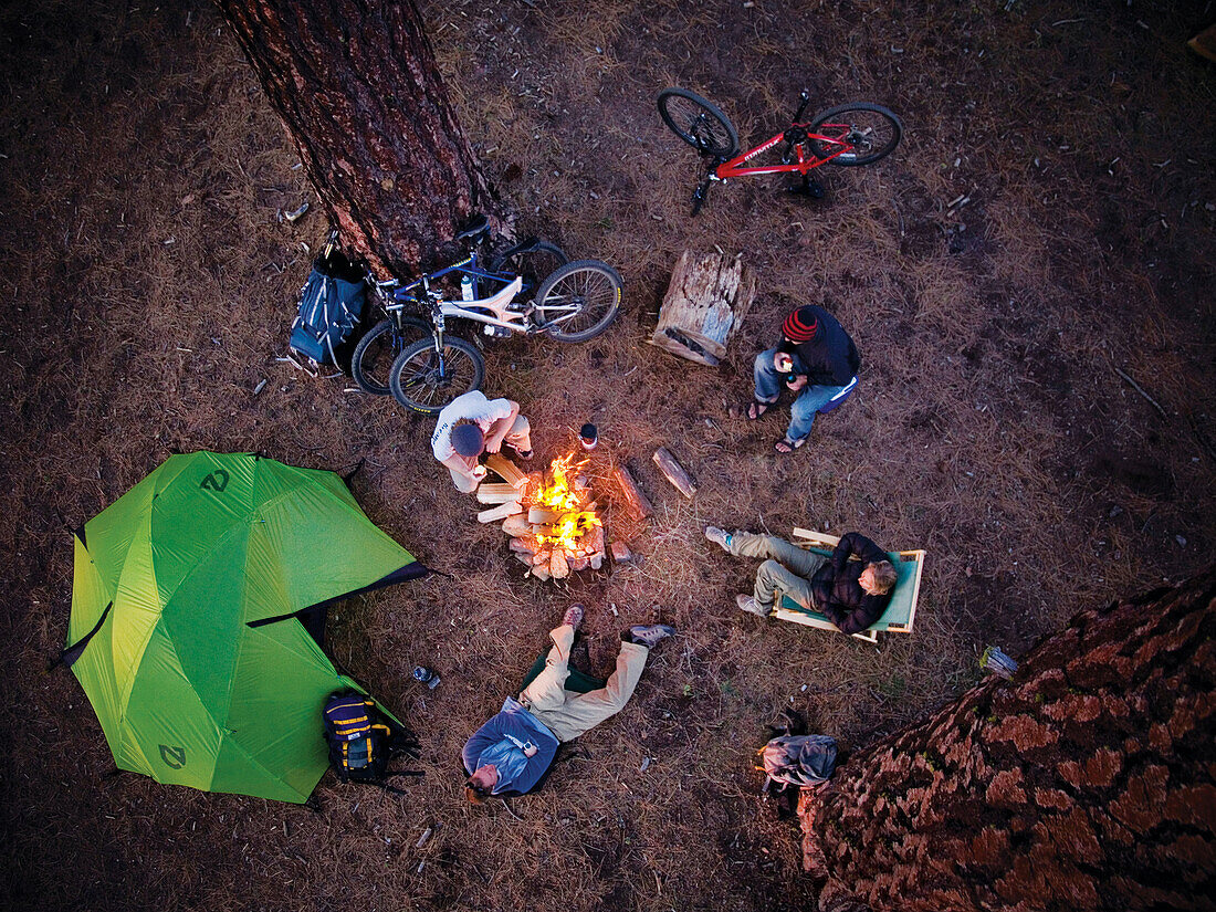 Group of friends gather outside their tent around the camp fire at a picnic on the beach.