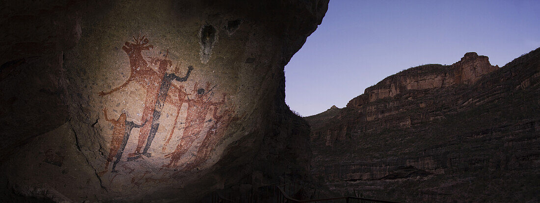 Large red-and-black human figures wearing elaborate headdresses dominate the mural at Cueva de La Flechas Cave of the Arrows, in the Sierra de San Francisco, Baja California Sur, Mexico. The cave painting site gets its name from two human figures pierced 