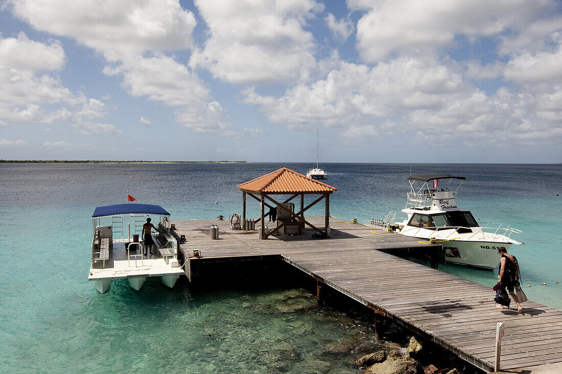 Unidentified scuba diver carries dive gear down the pier at Captain Don's Habitat in Bonaire, Netherlands Antilles, February 2, 2009.  The tranquil Caribbean Sea lets the awaiting dive boats rest calmly at the dock.