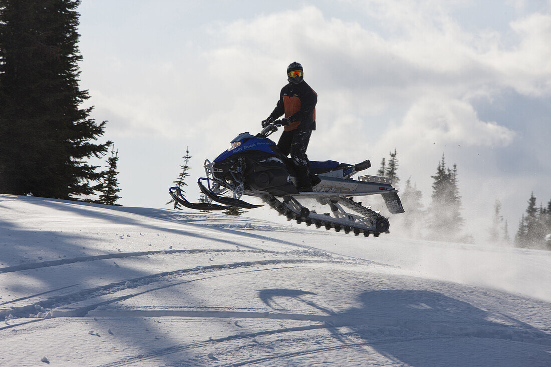 A man turns to look at the camera as he jumps his snowmobile in the air while riding on Owlshead Mountain above Sicamous in British Columbia, Canada.