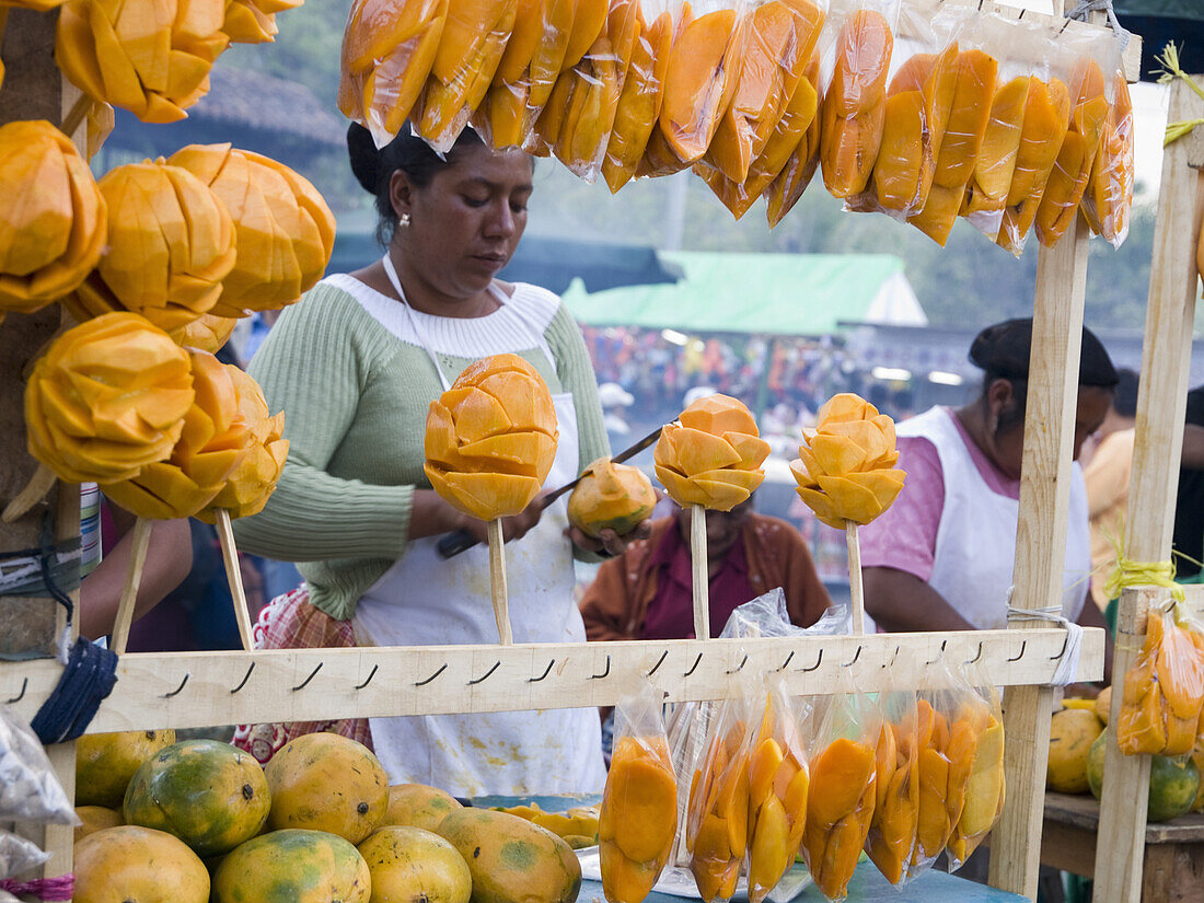 During a street festival, a woman cuts up mangoes to be eaten as street food snacks in San Bartolo, Sacatepequez, Guatemala.