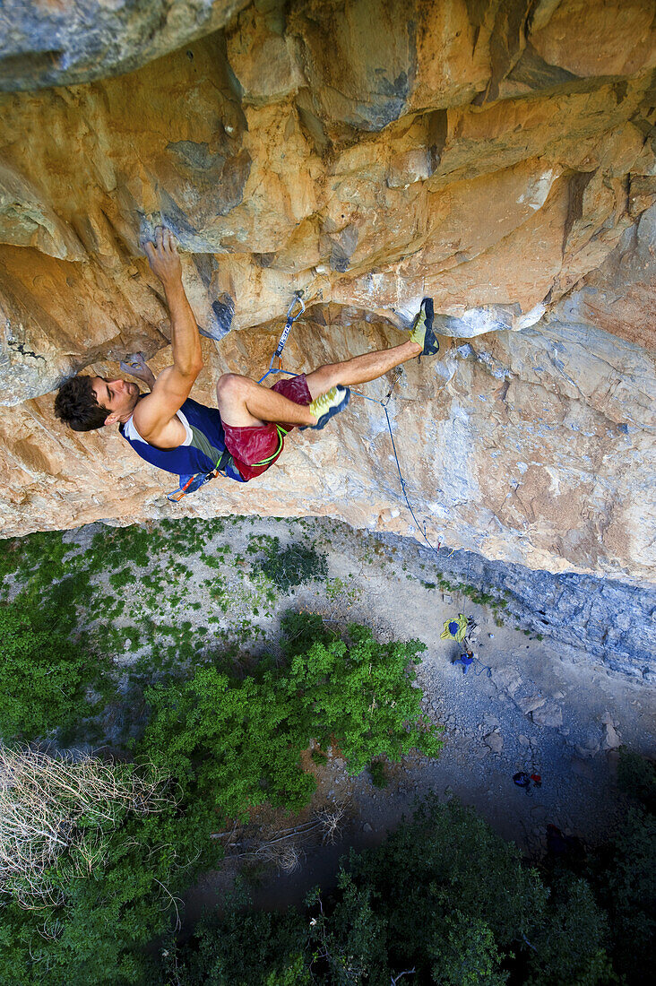 A rock climber in a blue tank top climbing a steep and technical route on yellow limestone at spring time in Rifle Colorado.