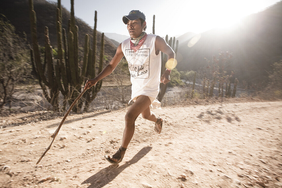A Tarahumara runner, runs on a dirt road using a stick as a pole during an ultra marathon in Urique, Chihuahua, Mexico.