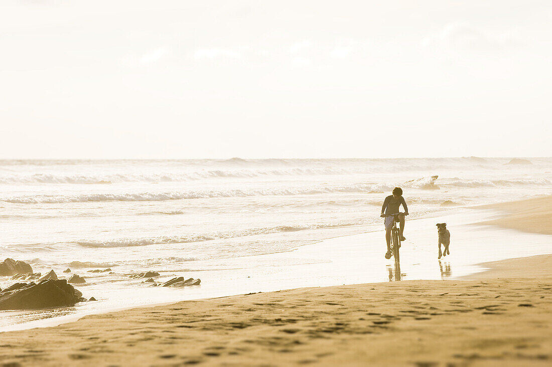 Nico Steele, age 14, rides his bicycle while Mancha the dog runs alongside on a quiet stretch of sandy beach in Troncones, Mexico on March 28, 2009.