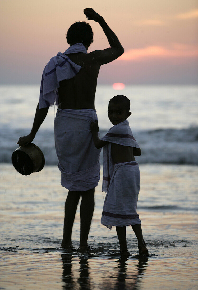 A Brahmani father and sun perform a ritual in the Arabian Sea during sunset in the holy Hindu pilgrimage village of Gokarna, Karnataka, India.