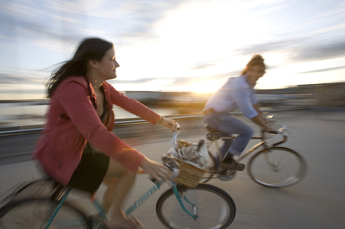 A young man and woman smile as they enjoy a sunny afternoon bike ride through an open street in Portland, ME. Motion Blur