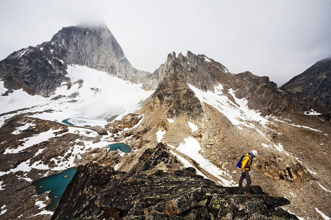 A man scrambling a ridge line on Eastpost spire in the Bugaboos.  Snow remains throughout the summer months in this high alpine environment.