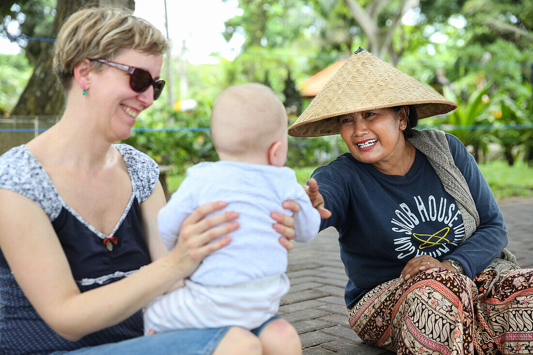 Balinese women, German mother with baby, playing, intercultural, meeting local people, locals, family travel in Asia, western baby, parental leave, MR, Sanur, Bali, Indonesia