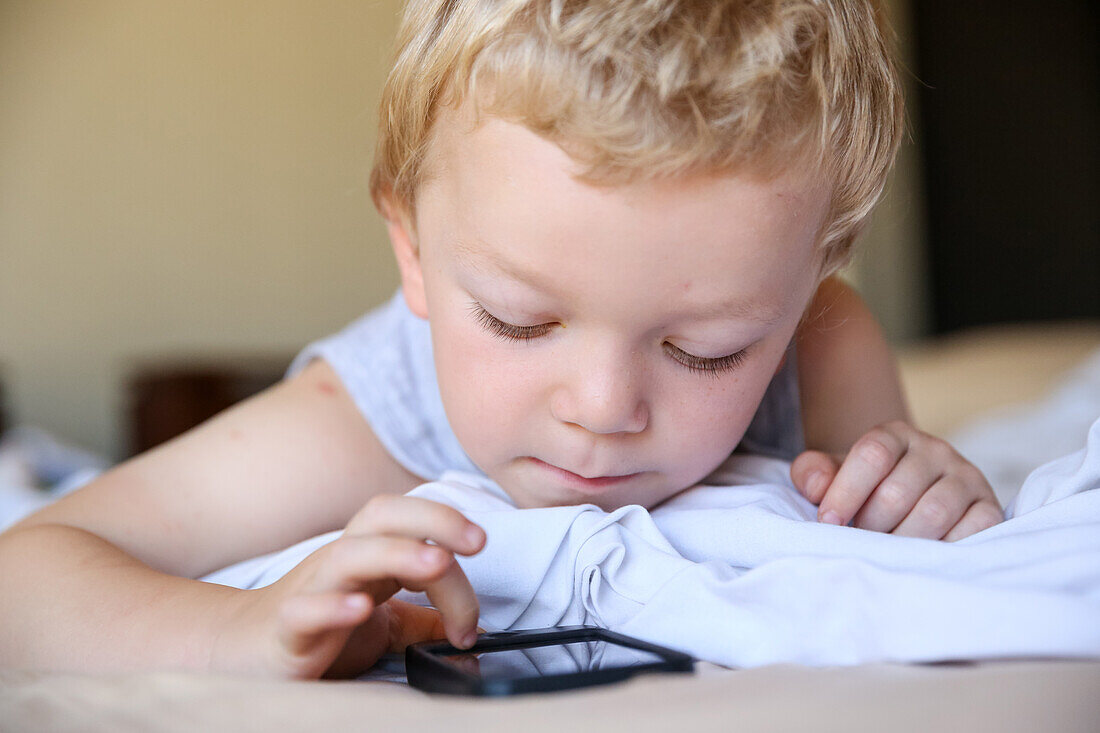 Little boy using a smartphone, lying on a bed, touchscreen