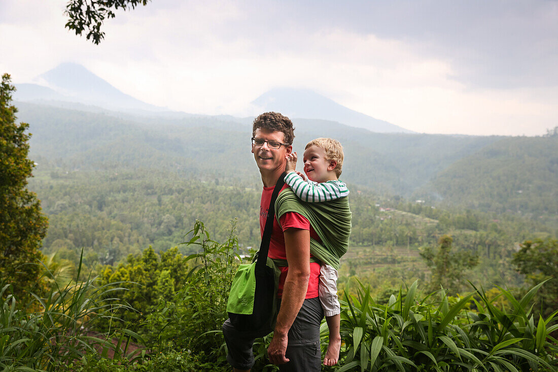 Father hiking with his son, boy 3 years old in a wrap on his back, forest, walking, parental leave, Munduk, Bali, Indonesia