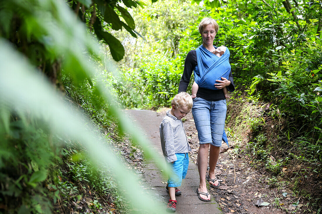 Mother hiking with her kids, baby 5 months, wrap, baby sling, son 3 years old, tropical rain forest, walking, family travel in Asia, parental leave, German, European, MR, Munduk, Bali, Indonesia