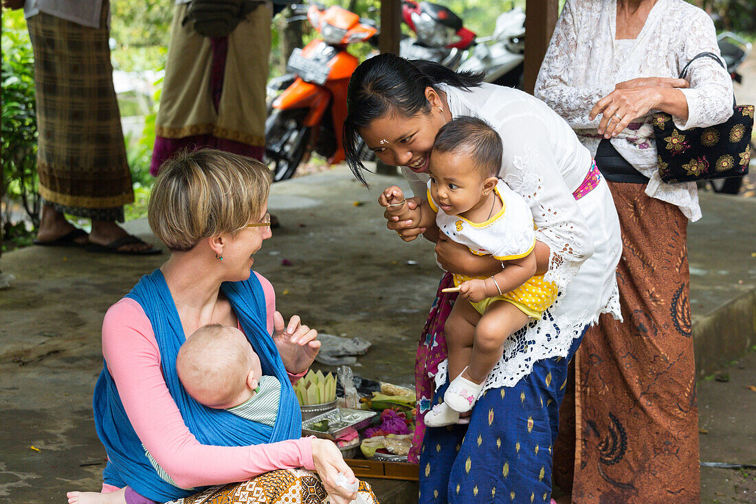 Balinese mother with her children playing with Baby of German mother, baby sling, wrap, baby sling at her mother, baby 5 months old, intercultural contact, meeting local people, locals, family travel in Asia, parental leave, German, European, MR, Munduk, 