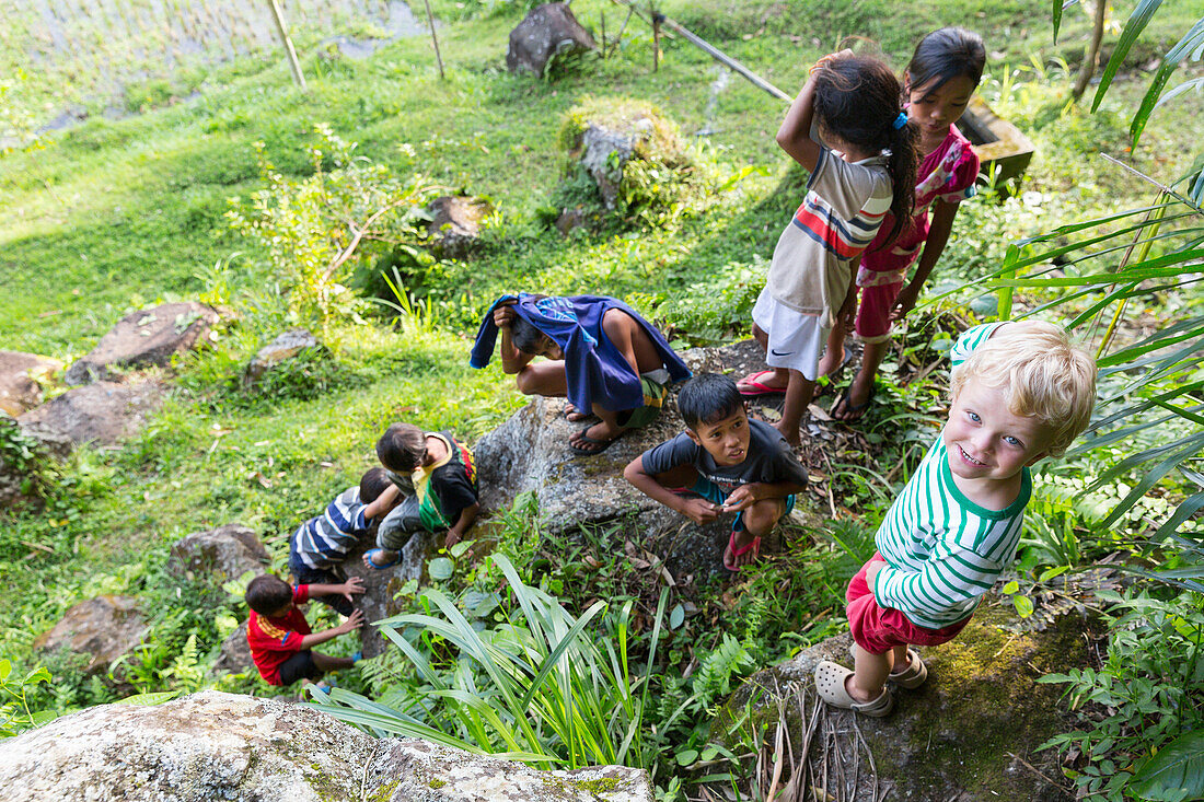 Deutscher Junge spielt mit indonesischen Kindern, klettern auf Felsen, auf dem Land, Dorf, Junge 3 Jahre, Kontakt mit Einheimischen, interkulturell, Ferien, Elternzeit in Asien, Europäer, Deutsche, Westler, Familie, MR, Tetebatu, Lombok, Indonesien