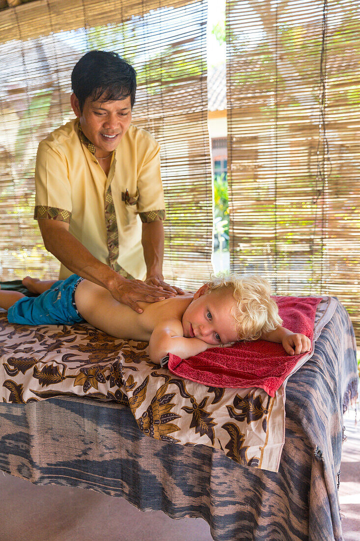Little boy getting back massage, Balinese masseur, boy 3 years old, wellness, hotel, intercultural contact, meeting local people, locals, Balinese holiday resort, family travel in Asia, parental leave, German, European, MR, Sidemen, Bali, Indonesia