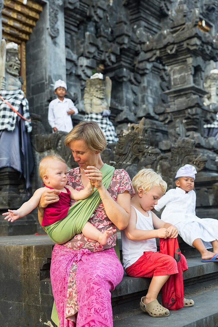 Mother with her children sitting on stairs, temple, baby 5 months old, baby sling, wrap, boy 3 years old, blond, temple Goa Lawah with bat cave, Balinese people, temple ceremony, intercultural contact, meeting local people, locals, family travel in Asia, 