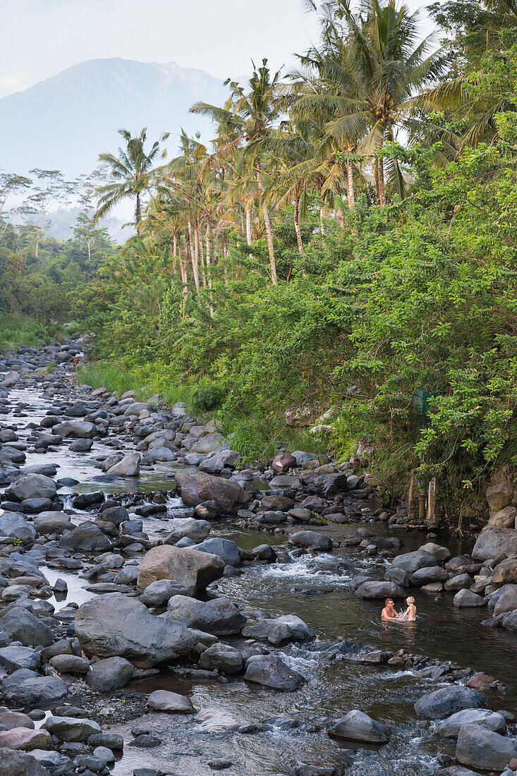 Father and son taking a bath in a river, riverbed, rocks, stones, local Balinese taking baths here, trees, local custom, intercultural, boy 3 years old, family on holiday, family travel in Asia, parental leave, German, European, MR, Sidemen, Bali, Indones