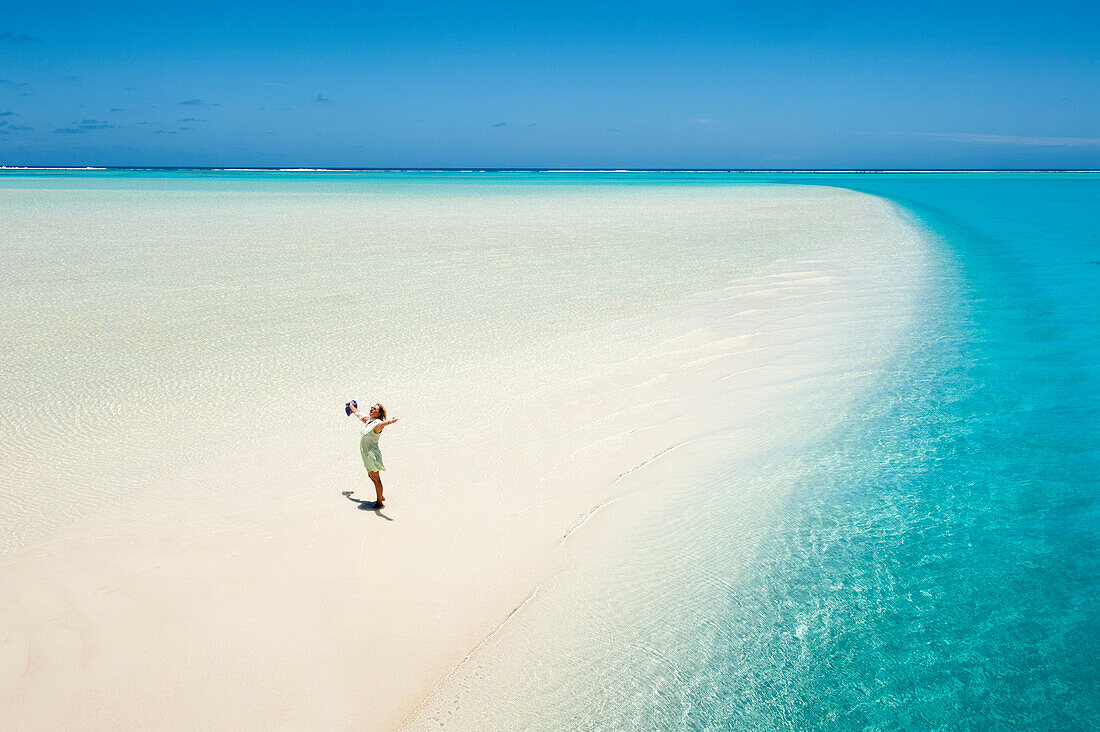 Eine Frau steht auf einer Sandbank der One Foot Island in der Lagune von Aitutaki und reißt vor Glückseligkeit ihre Arme in die Höhe, Aitutaki, Cook-Inseln, Südpazifik