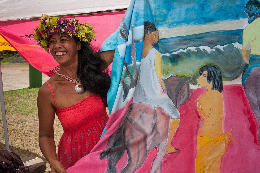 Polynesische Frau zeigt Pareu-Tuch mit Bemahlung im Gauguin-Stil auf einem Markt, Atuona, Hiva Oa, Marquesas-Inseln, Französisch Polynesien, Südpazifik