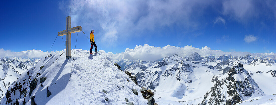 Female back-country skier standing beside summit cross of Piz Buin, Silvretta Range, Lower Engadin, Engadin, Canton of Graubuenden, Switzerland