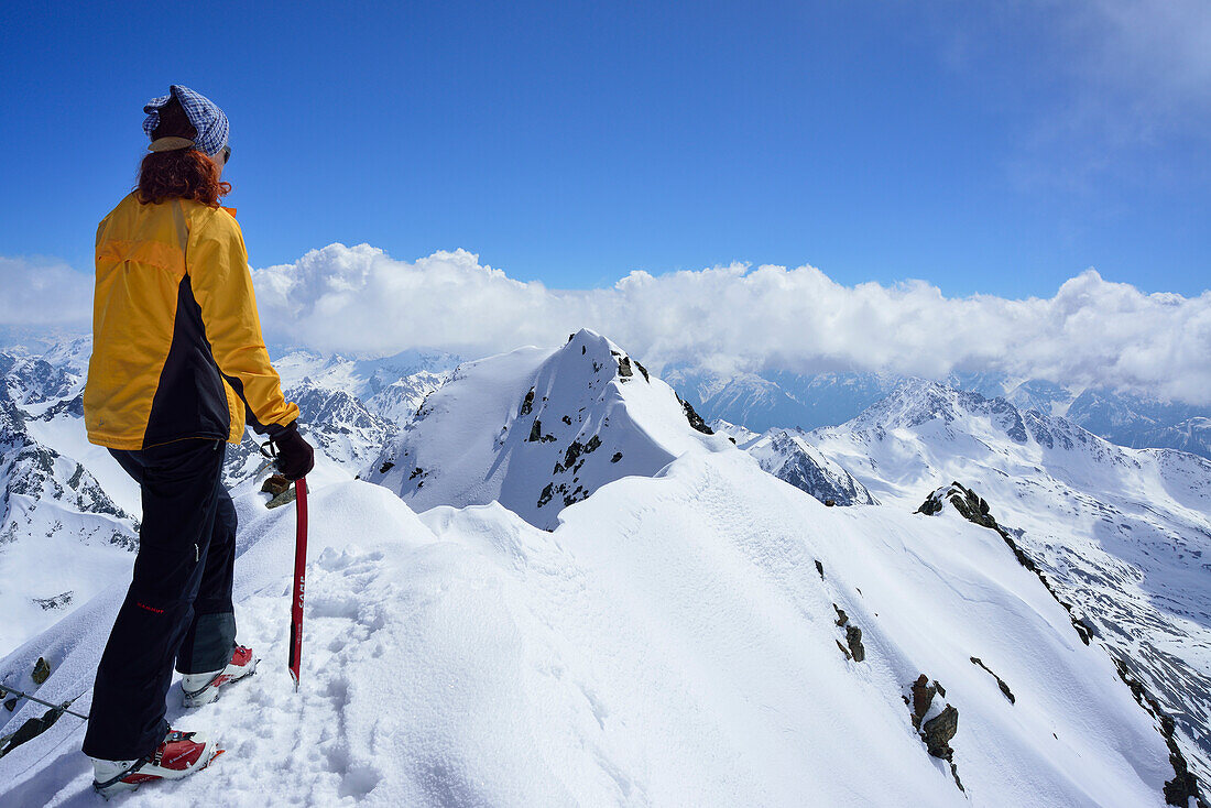 Female back-country skier at summit of Piz Buin and looking at mountain panorama, Silvretta Range, Lower Engadin, Engadin, Grisons, Switzerland