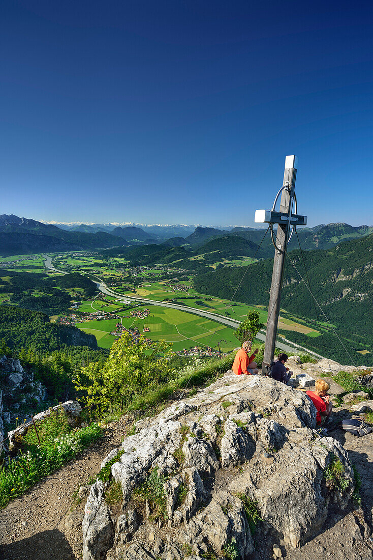 Three hikers sitting at summit cross on Kranzhorn, view over Inn valley, Chiemgau Alps, Tyrol, Austria