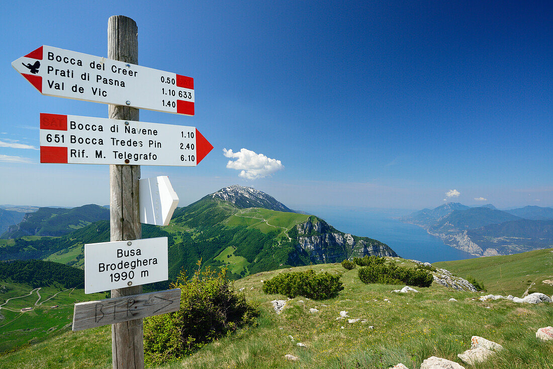 Signpost, Monte Baldo and lake Garda in background, Monte Altissimo, Garda Mountains, Trentino, Italy
