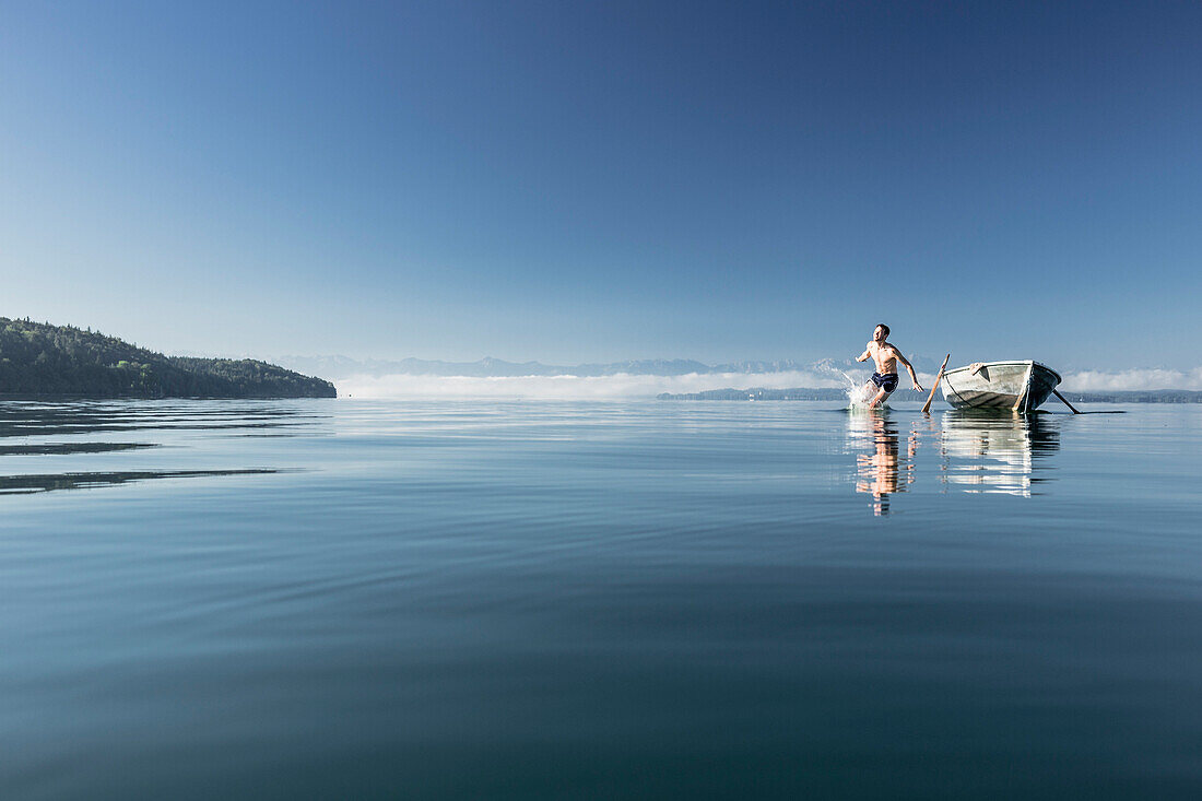 Man jumping into lake Starnberg, the Alps with mount Zugspitze in early morning fog, Berg, Upper Bavaria, Germany