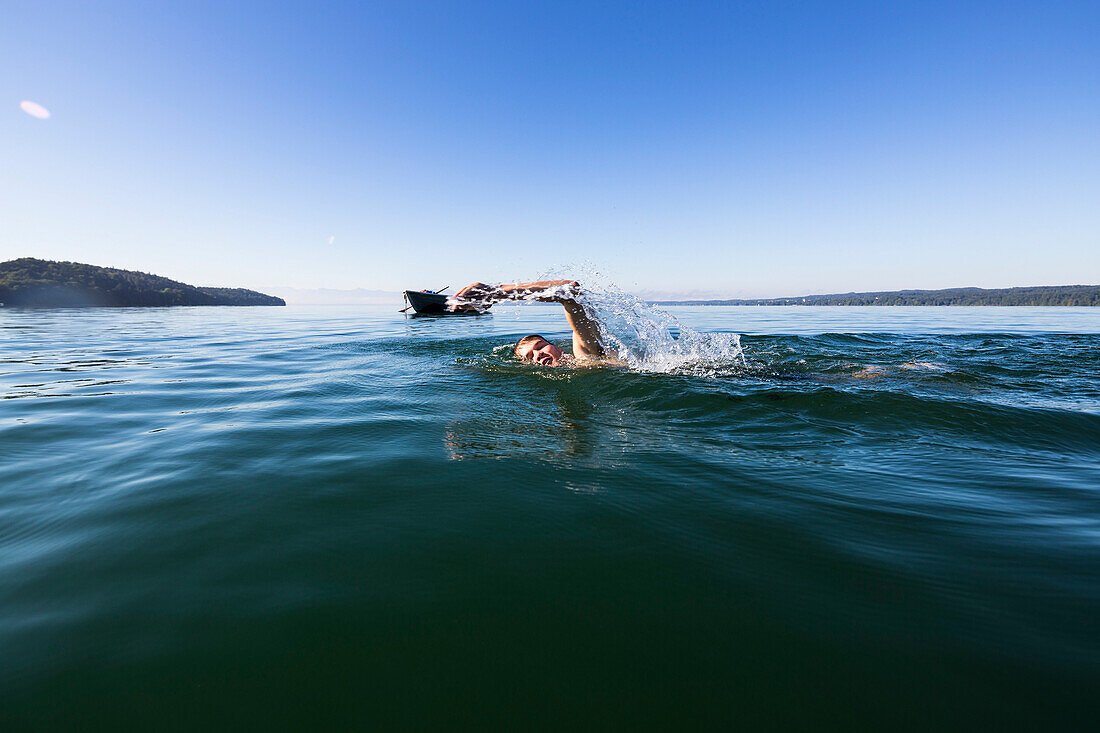 Man swimming in lake Starnberg, the Alps with mount Zugspitze in early morning fog, Berg, Upper Bavaria, Germany