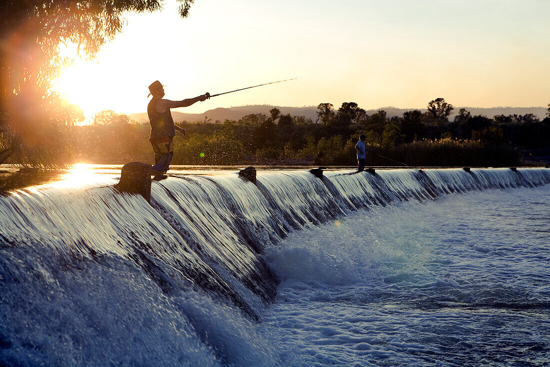 Angler auf dem Wehr der Parry Creek Road über den Ord River bei Sonnenuntergang, nahe Kununurra, Western Australia, Australien