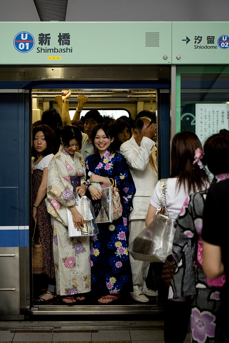 Ein überfüllter U-Bahn Waggon mit zwei lachenden modernen Geisha Mädchen, Shinbashi Station, Tokio, Region Kanto, Honshu, Japan