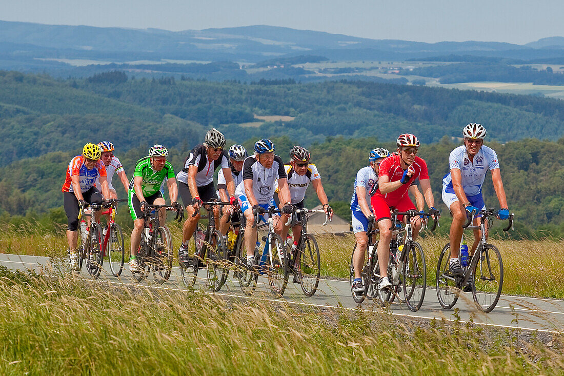 A group of cyclists cycling up a hill with Frankenberger Land behind, Frankenau, Hesse, Germany, Europe