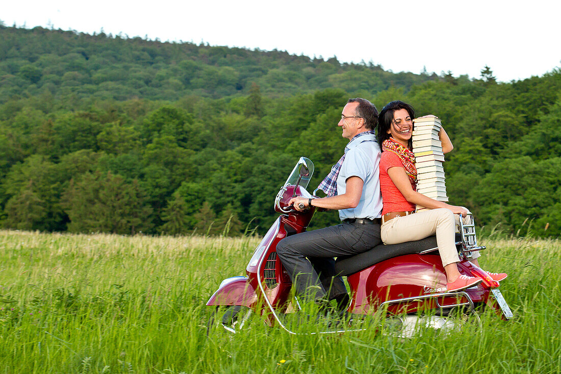 A man and a woman transport a stack of books on a red Vespa scooter, Bad Wildungen, Hesse, Germany, Europe