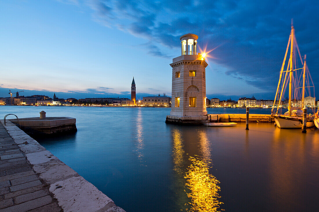 Kleiner Leuchtturm an der Einfahrt zur Marina der Isola di San Giorgo Maggiore Insel am San Marco Basin mit Blick auf Campanile di San Marco Turm und Dogenpalast am Markusplatz in der Dämmerung, Venedig, Venetien, Italien, Europa