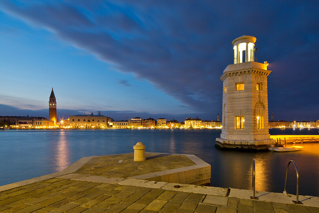 Kleiner Leuchtturm an der Einfahrt zur Marina der Isola di San Giorgo Maggiore Insel am San Marco Basin mit Blick auf Campanile di San Marco Turm und Dogenpalast am Markusplatz in der Dämmerung, Venedig, Venetien, Italien, Europa