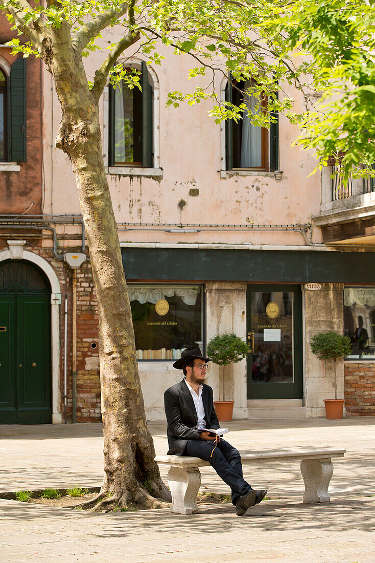 A jew sitting on a bench under a tree at Campo del Ghetto Nuovo in Ghetto Vecchio, Venice, Veneto, Italy, Europe