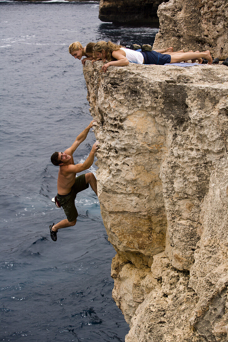 Brett Lowell shows off to the ladies above him while deep water soloing / rock climbing at Cala Sa Nau, Mallorca, Spain. Kim Miller, Catherine Brunel-Guitton and Melissa Lacasse watch from the cliff top above.