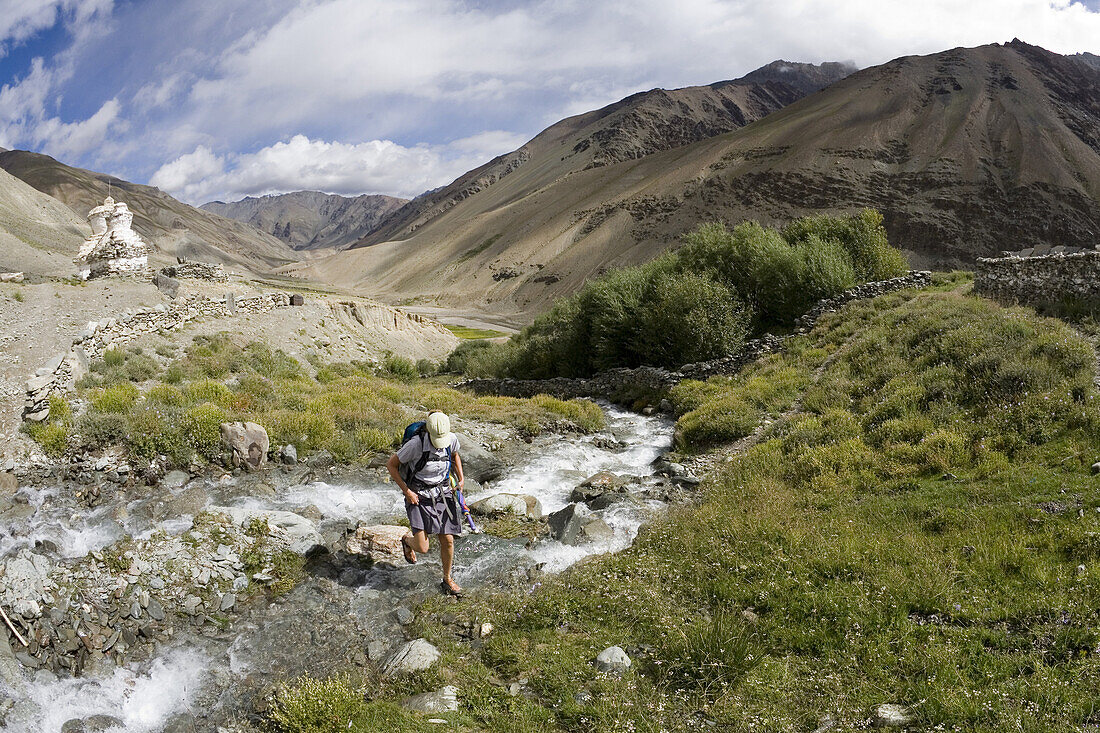 Caucasian woman crosses creek during trek in Zanskar Mountain Range of Ladakh, northern India.  The high altitude area is popular with trekkers because of its Buddhist and Muslim cultural heritage and its stunning scenery