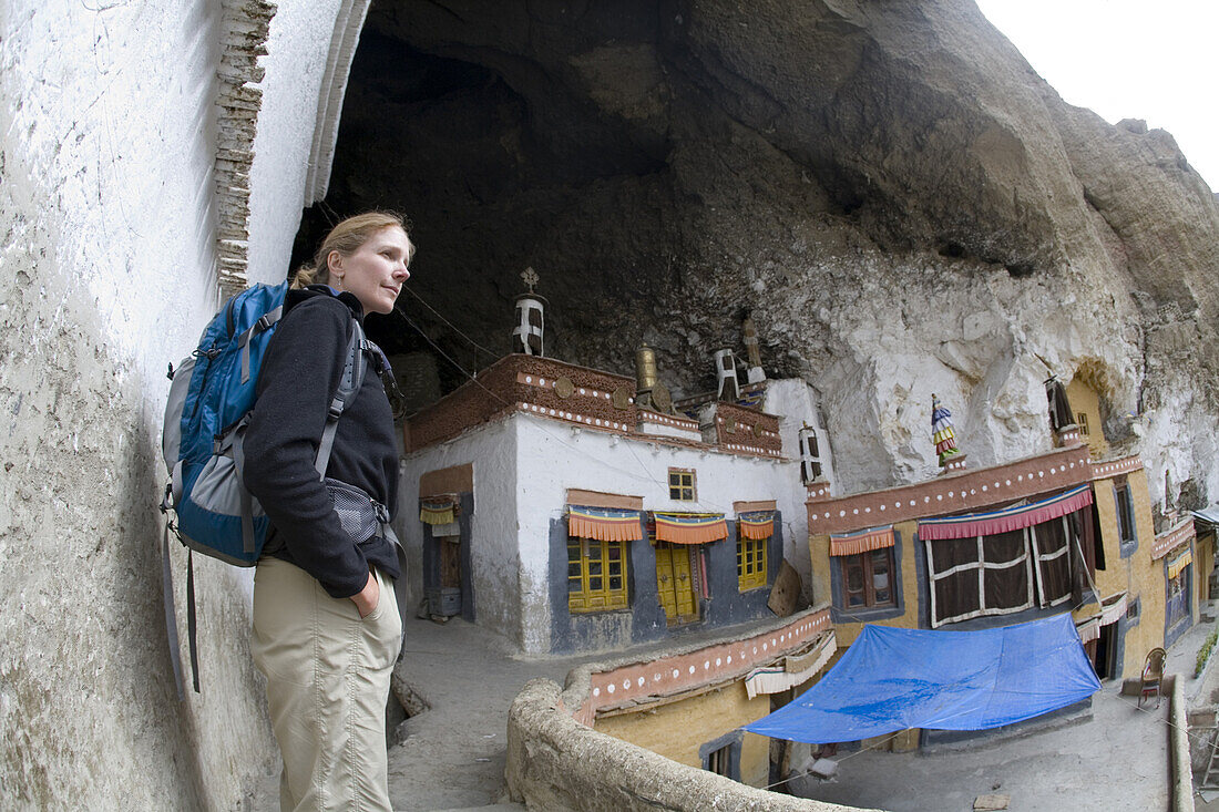 Caucasian woman trekker with backpack enjoys view of Phuktal Monastery during trek in Zanskar Mountains of northern India.  The area is popular with trekkers because of its rugged mountains and Buddhist and Muslim cultures.