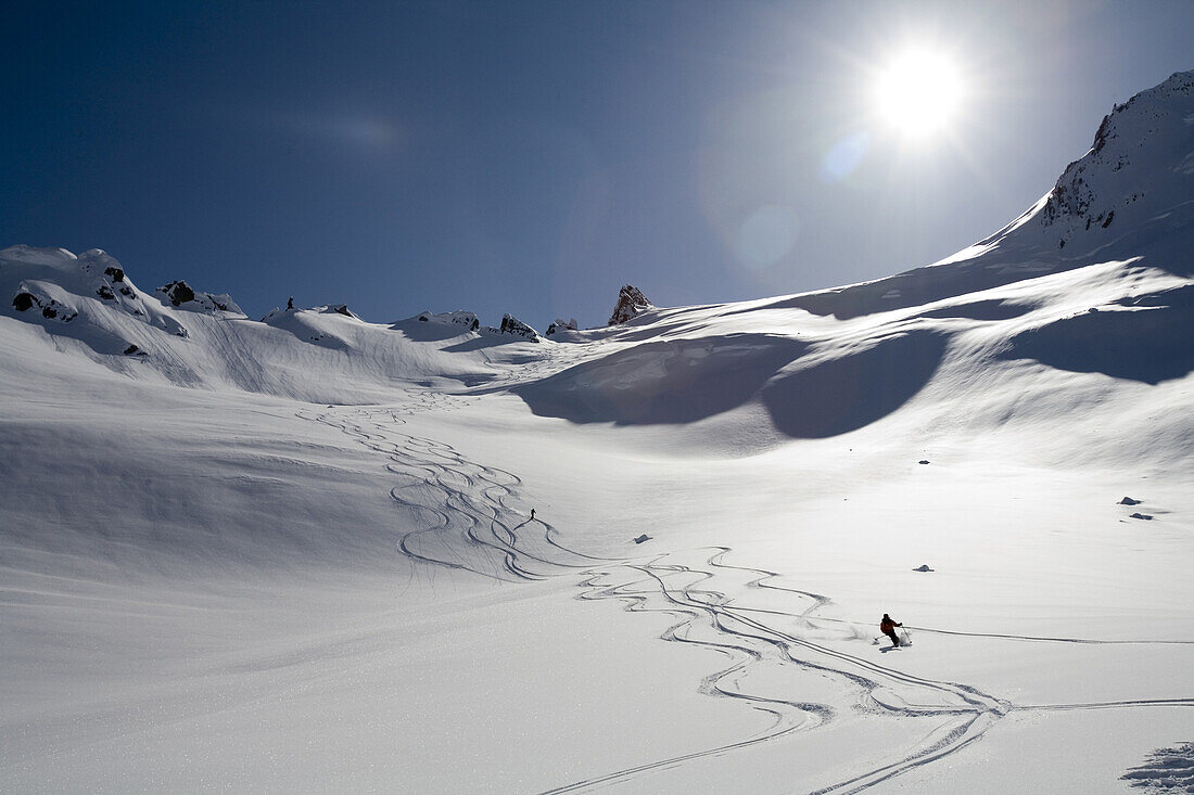 Man skis down hill in Alaska backcountry near Alaska Canada border on sunny blue sky day. Back lit,.