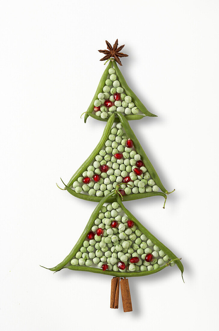 Fresh green beans, dried peas, pomegranate seeds, cinnamon sticks, and star anise arranged to look like a decorated christmas tree.