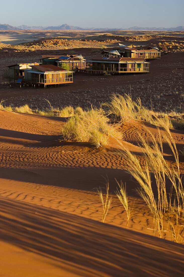 Wolwedans Dune Lodge chalets glow in early moring light. The chalets are surrounded by the burnt orange dunes of the Namib Rand Nature Reserve, Namibia.