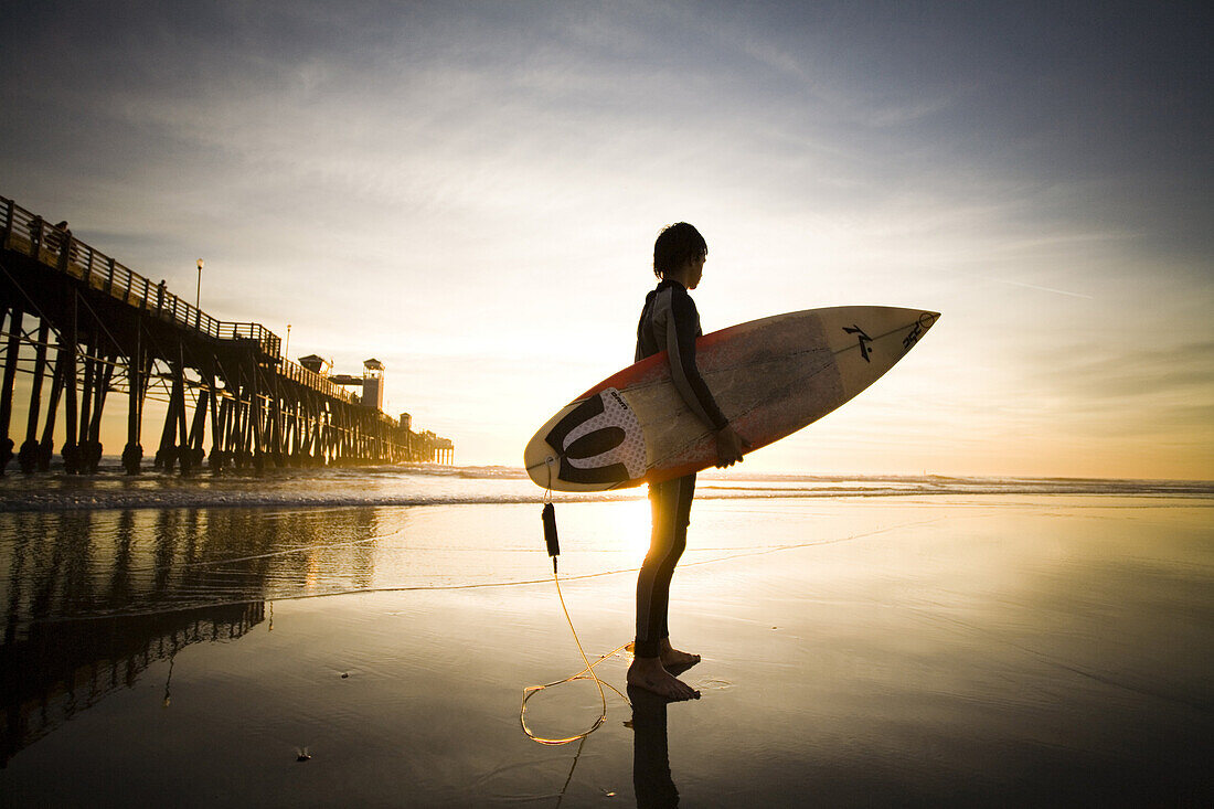 A young surfer stands on the beach at sunset in Oceanside, CA.