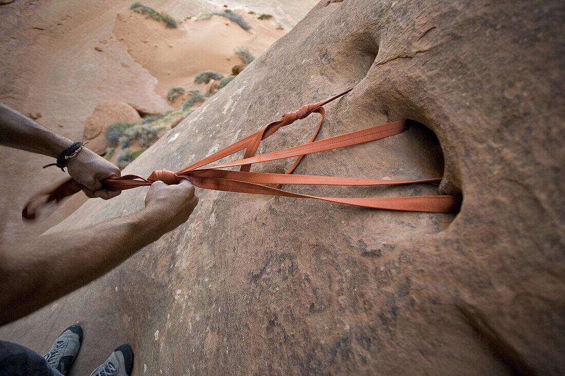 Setting up a rappel from natural holes in the rock in a canyon in Arches National Park, Utah.