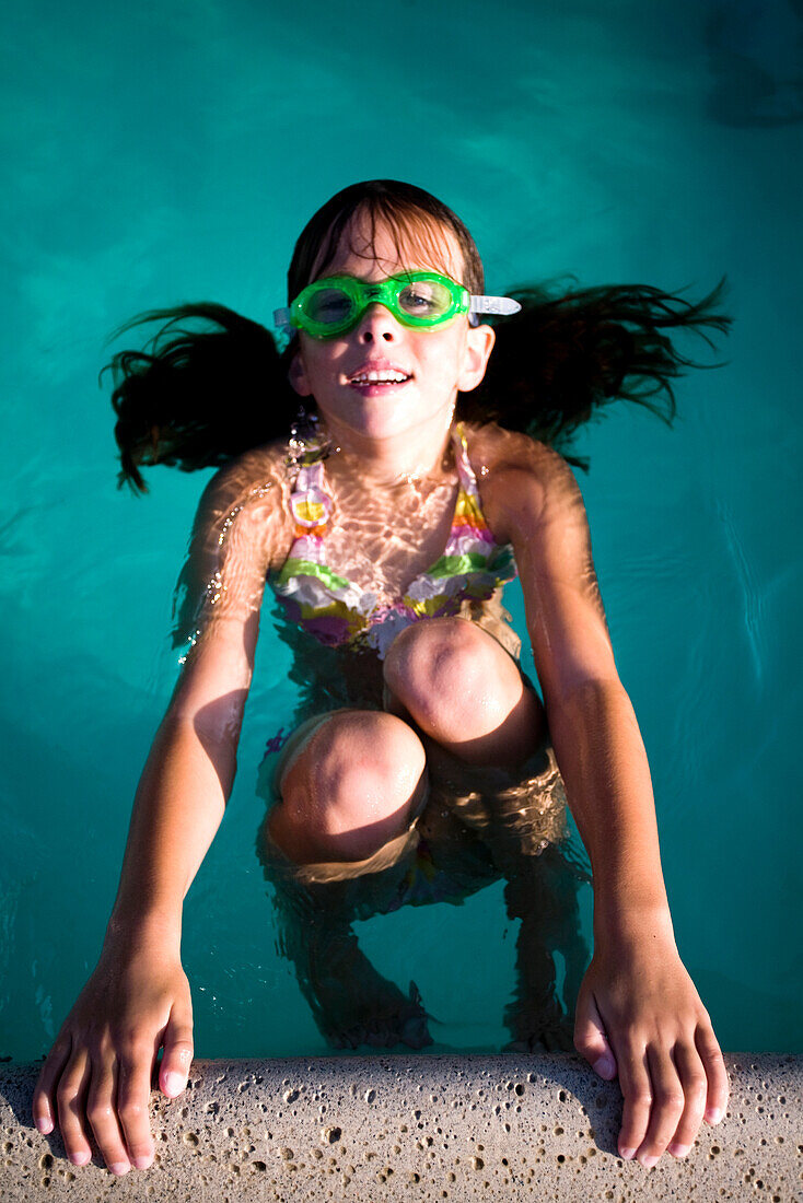 A girl in goggles floats in the water at a pool party.