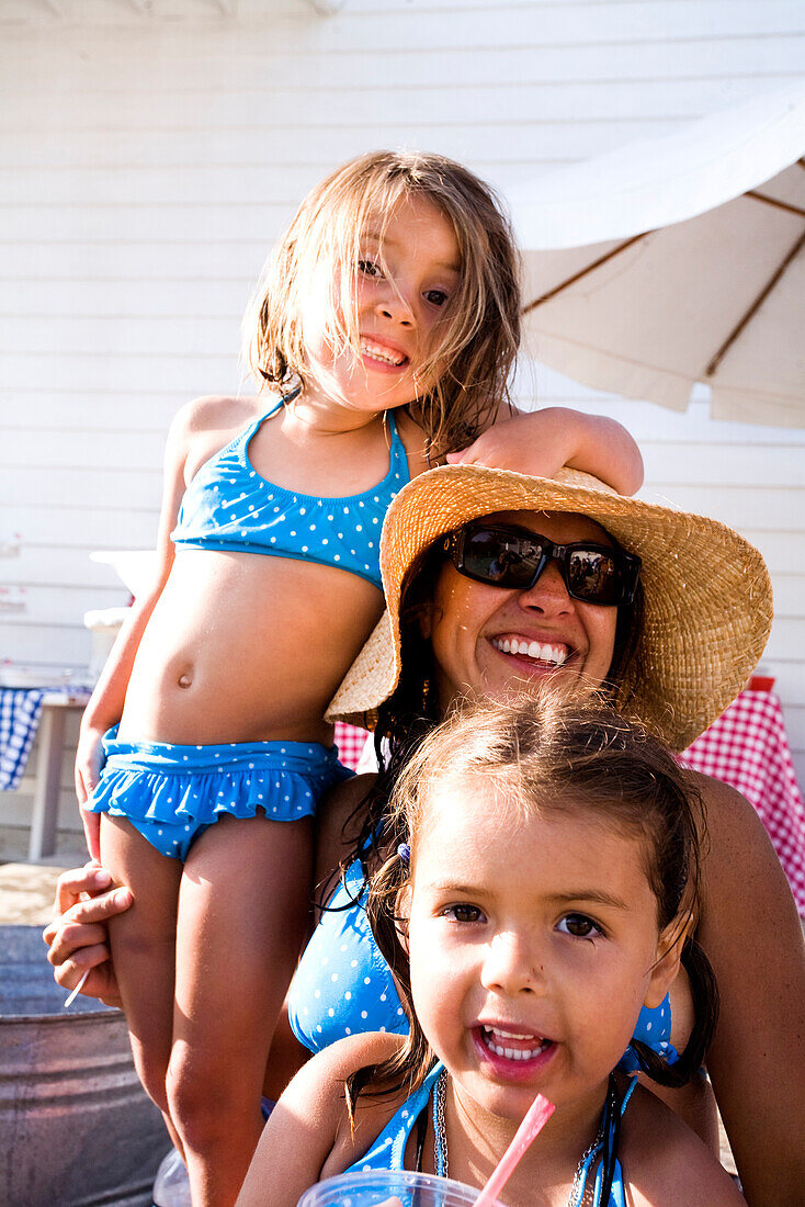 Mom and two little girls smile for the camera at a pool party.