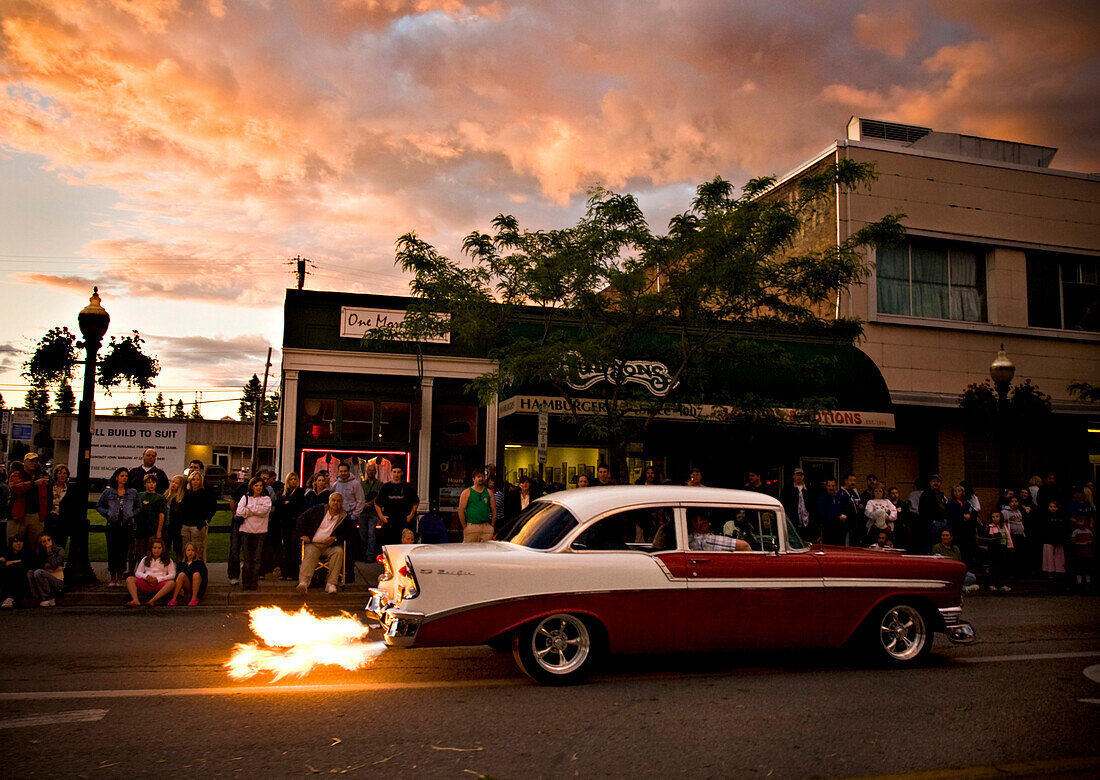 Spectators stand along a street watching a vintage car with a flaming exhaust in Coeur d'Alene, Idaho.