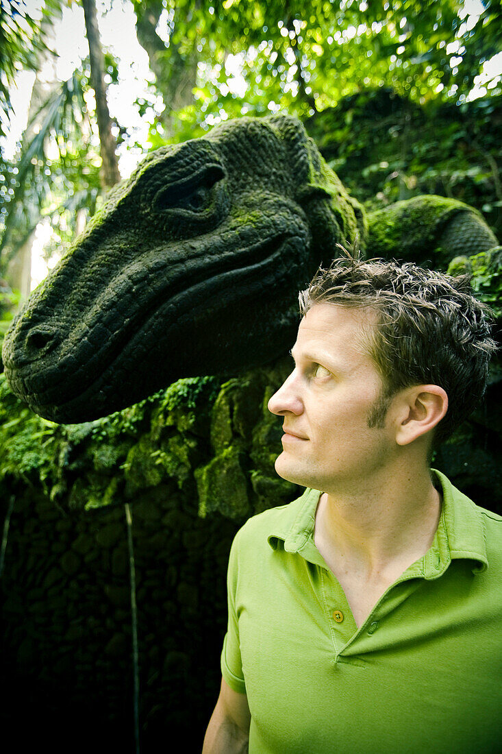 Aaron Gulley faces a sculpture of a giant Komodo Dragon covered in moss at the Holy Bathing Temple along the sacred Monkey Forest Road in Ubud, Bali Indonesia.