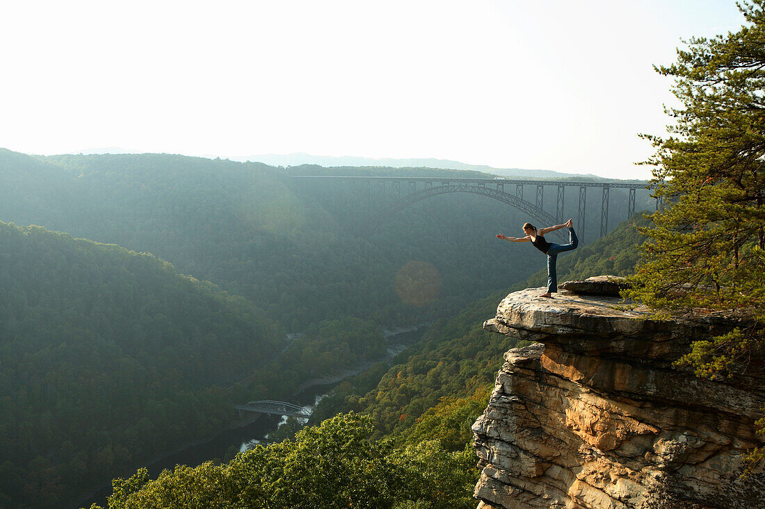 Sarah Chouinard enjoys a late afternoon yoga session standing bow pose, atop the Bosnian Buttress along the rim of the New River Gorge near Fayetteville, WV