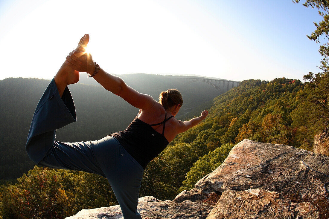 Sarah Chouinard genießt eine Yoga-Sitzung am späten Nachmittag in stehender Bogenhaltung auf dem Bosnian Buttress am Rande der New River Gorge bei Fayetteville, WV