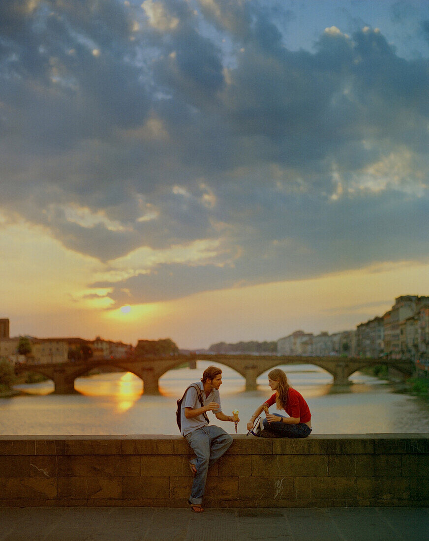 A young couple eating gelati on a bridge over The Arno River, Florence, Italy